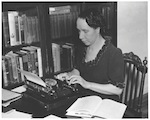 A woman using a typewriter near a bookcase